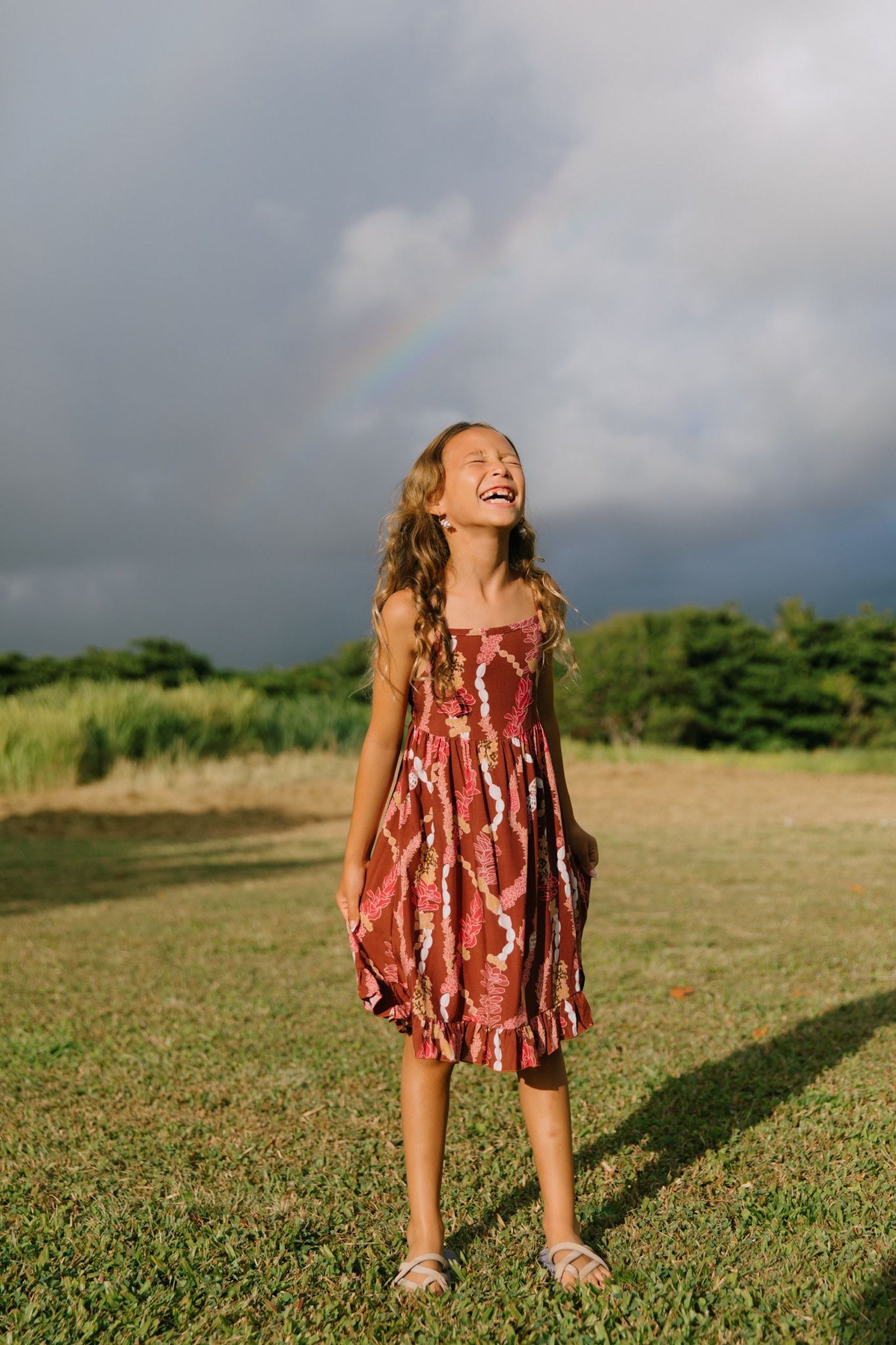 little girl wearing a red-brown tie back dress with ruffle hem and lei print