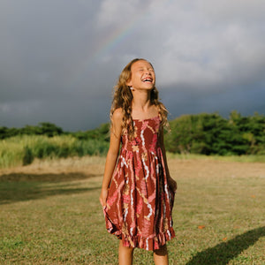 little girl wearing a red-brown tie back dress with ruffle hem and lei print