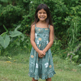 little girl wearing lush green tie back dress with puakenikeni print