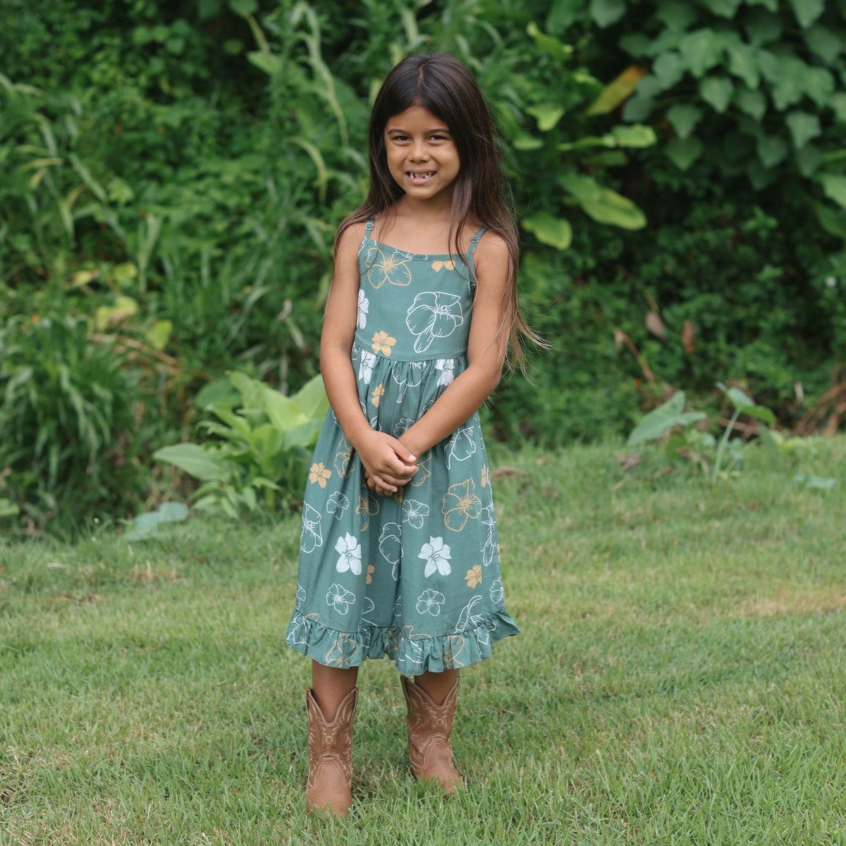 little girl wearing lush green tie back dress with puakenikeni print