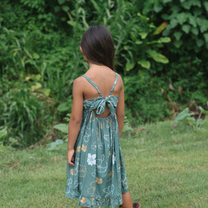 little girl wearing lush green tie back dress with puakenikeni print
