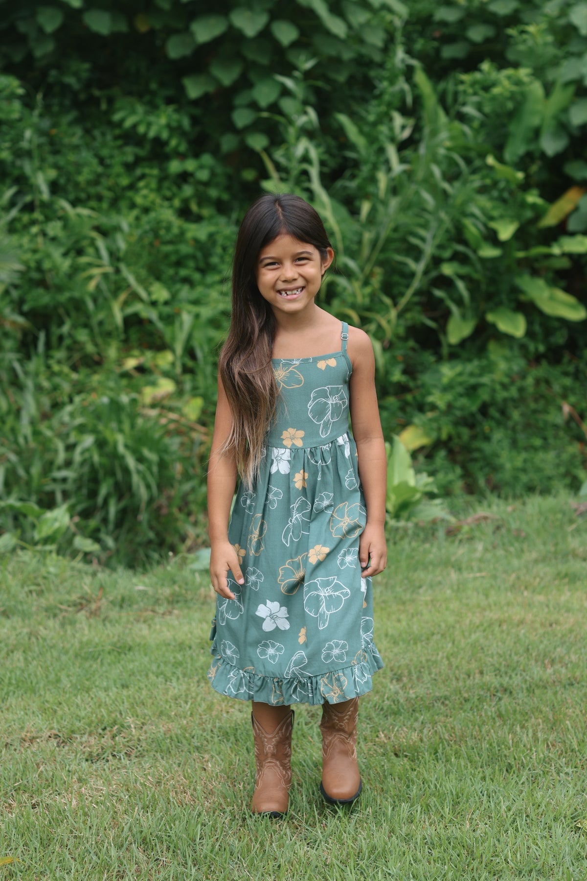 little girl wearing lush green tie back dress with puakenikeni print