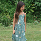 little girl wearing lush green tie back dress with puakenikeni print