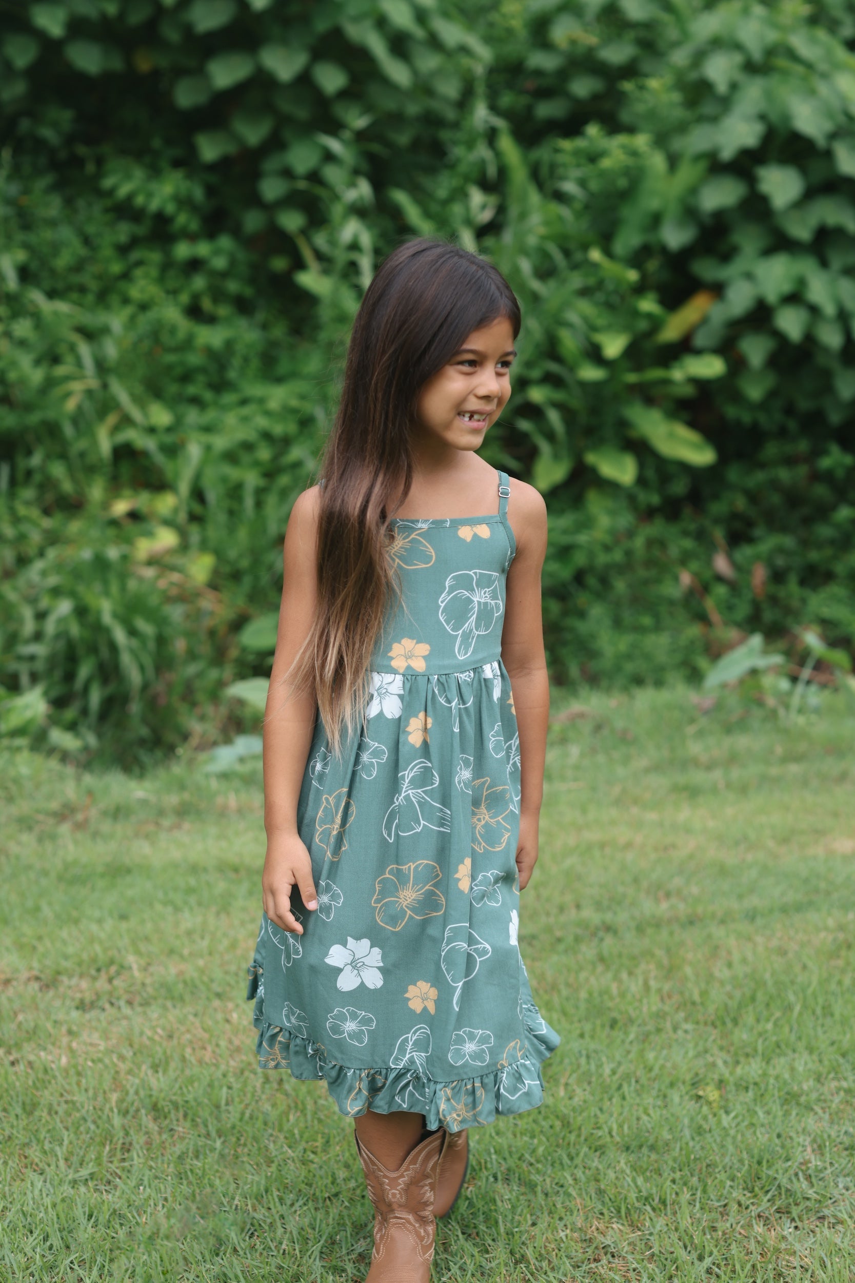 little girl wearing lush green tie back dress with puakenikeni print