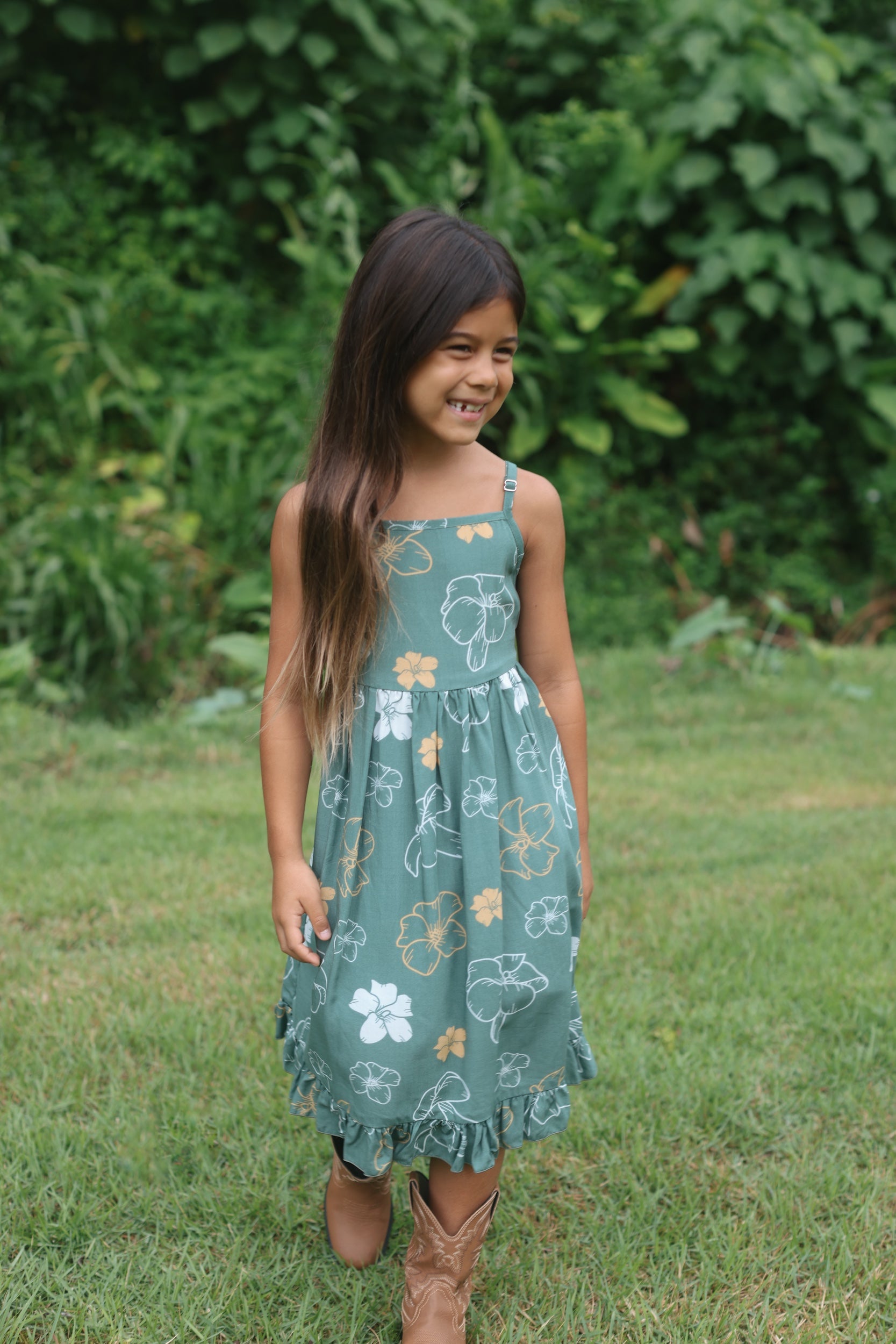 little girl wearing lush green tie back dress with puakenikeni print