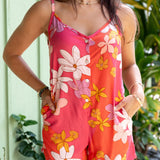 woman with brown hair wearing a bright pink spaghetti strap romper with retro flower print