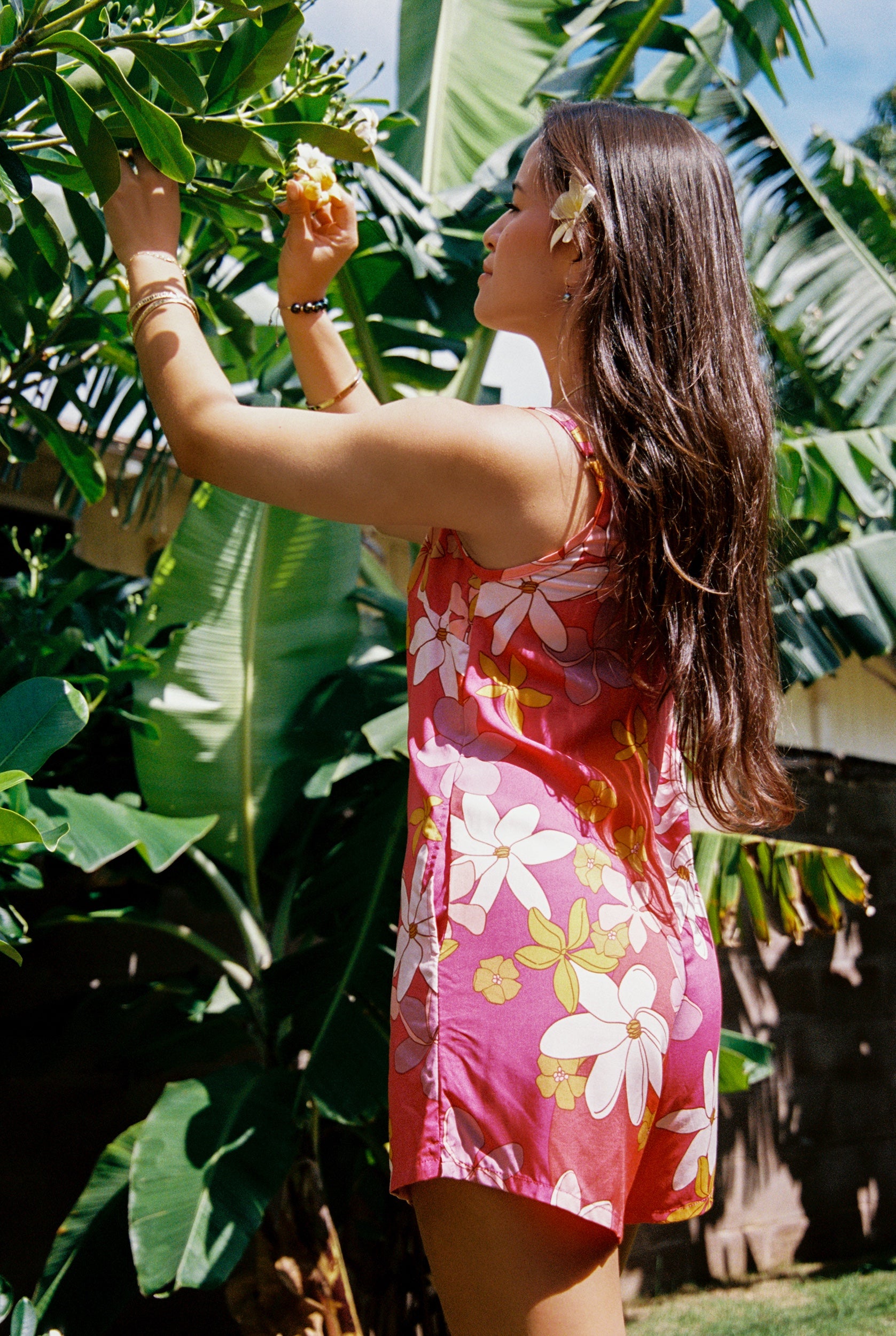 woman with brown hair wearing a bright pink spaghetti strap romper with retro flower print