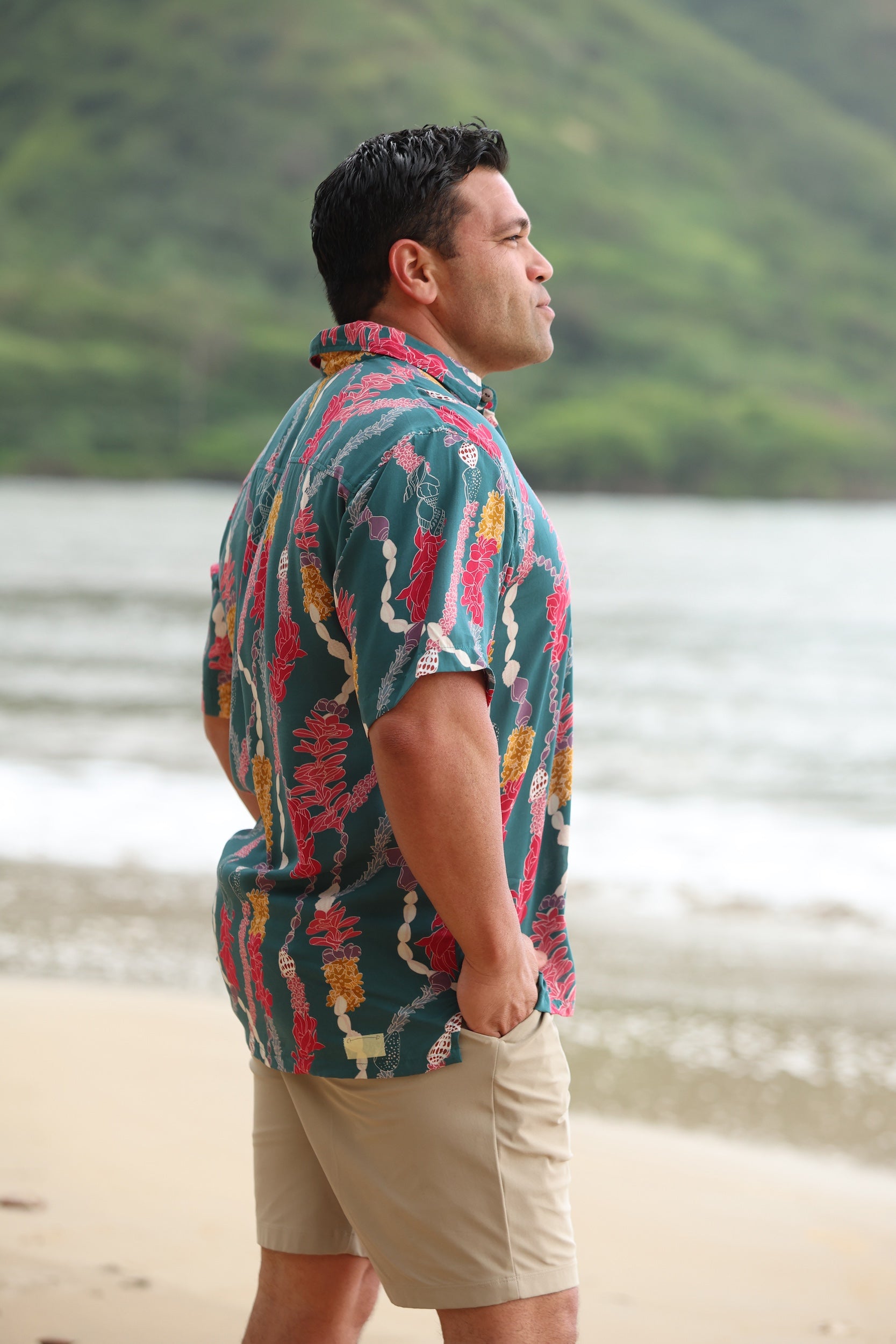 man with brown hair wearing dark teal aloha button up shirt with shell and lei print