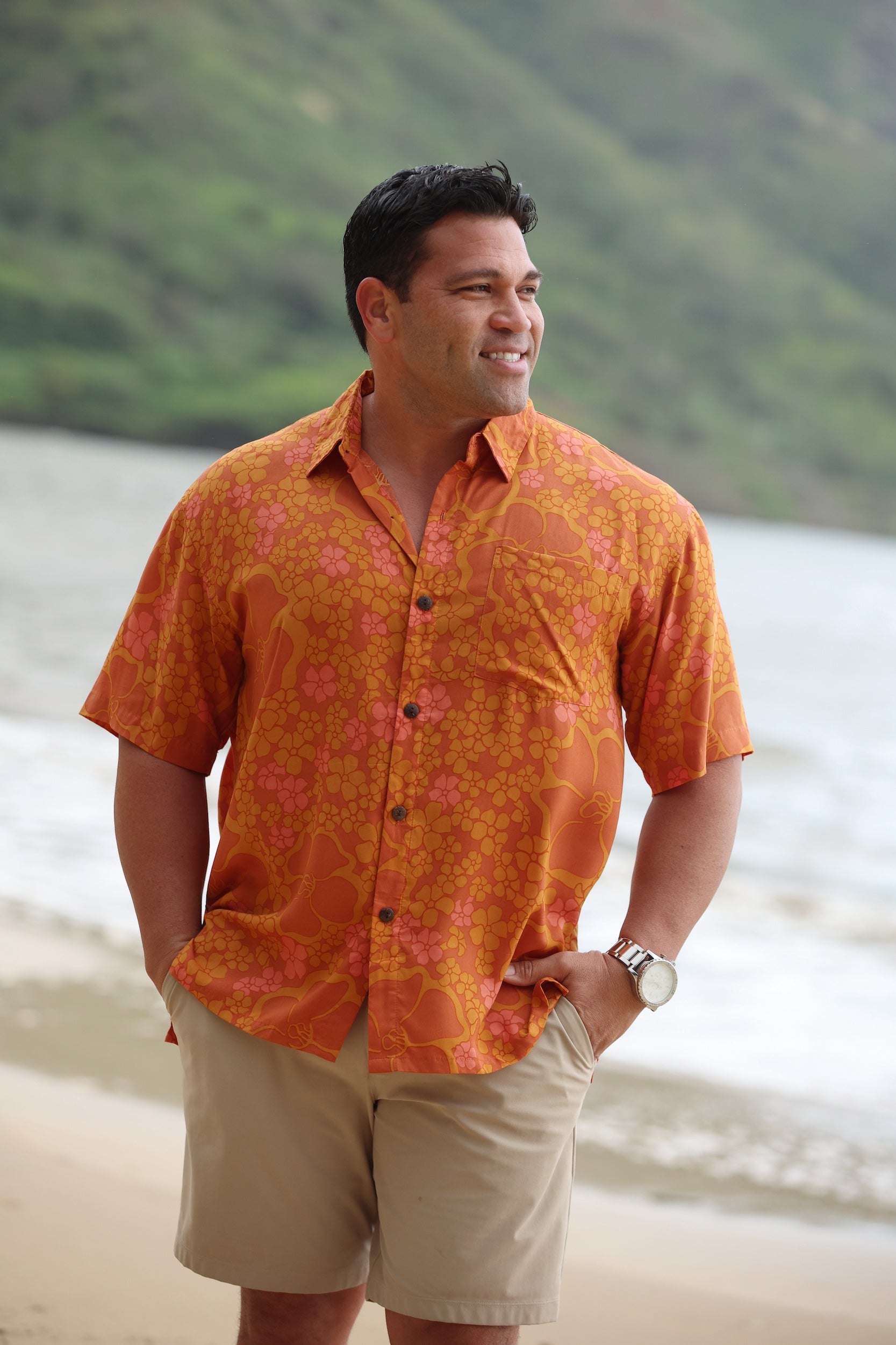 man with brown hair wearing an orange aloha button up shirt with puakenikeni print