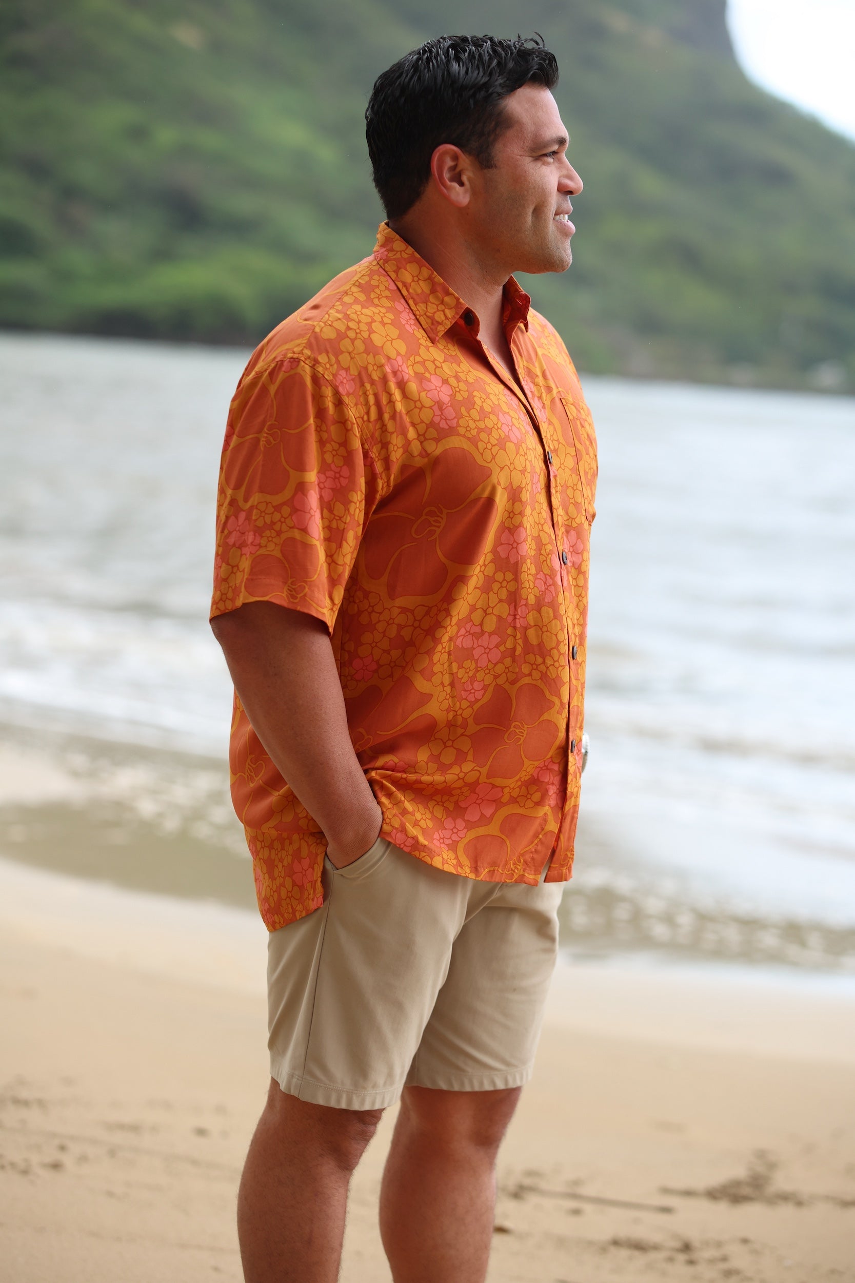 man with brown hair wearing an orange aloha button up shirt with puakenikeni print