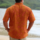 man with brown hair wearing an orange aloha button up shirt with puakenikeni print
