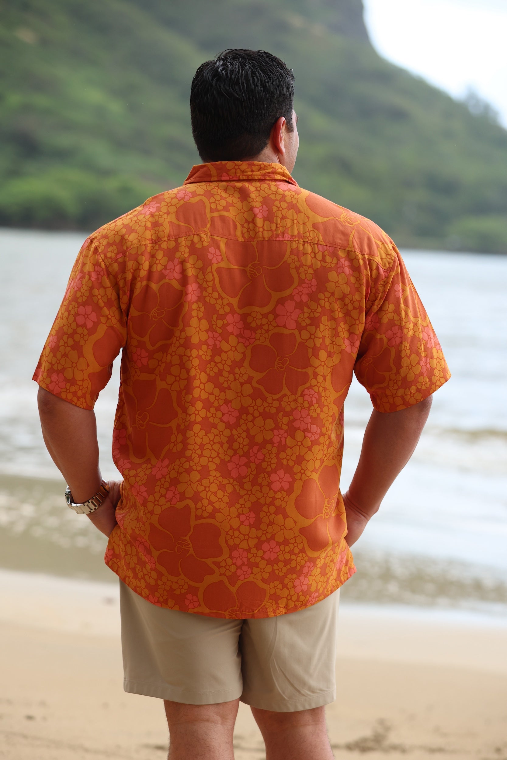 man with brown hair wearing an orange aloha button up shirt with puakenikeni print