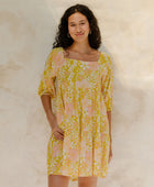 Woman in short flowy tiered dress with 3/4 sleeves in white and peach floral print with yellow ground.