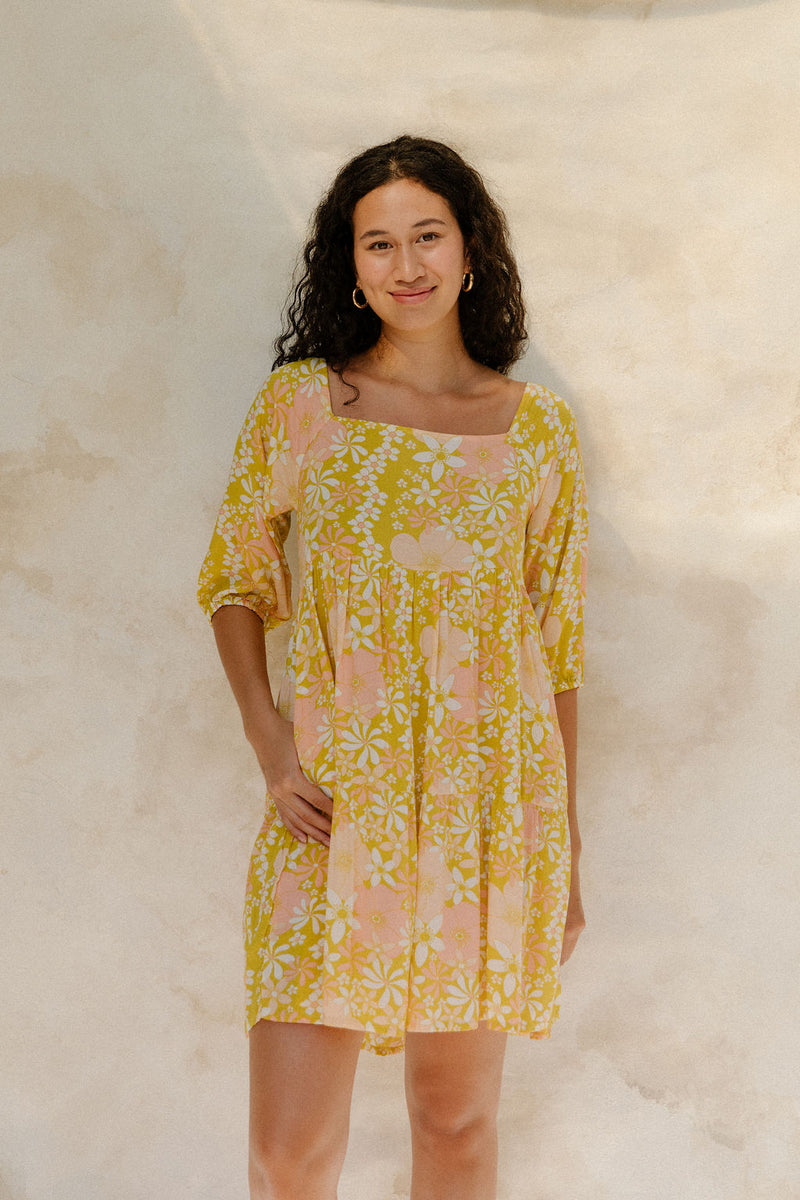 Woman in short flowy tiered dress with 3/4 sleeves in white and peach floral print with yellow ground.