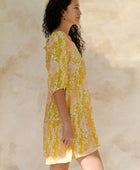 Woman in short flowy tiered dress with 3/4 sleeves in white and peach floral print with yellow ground.