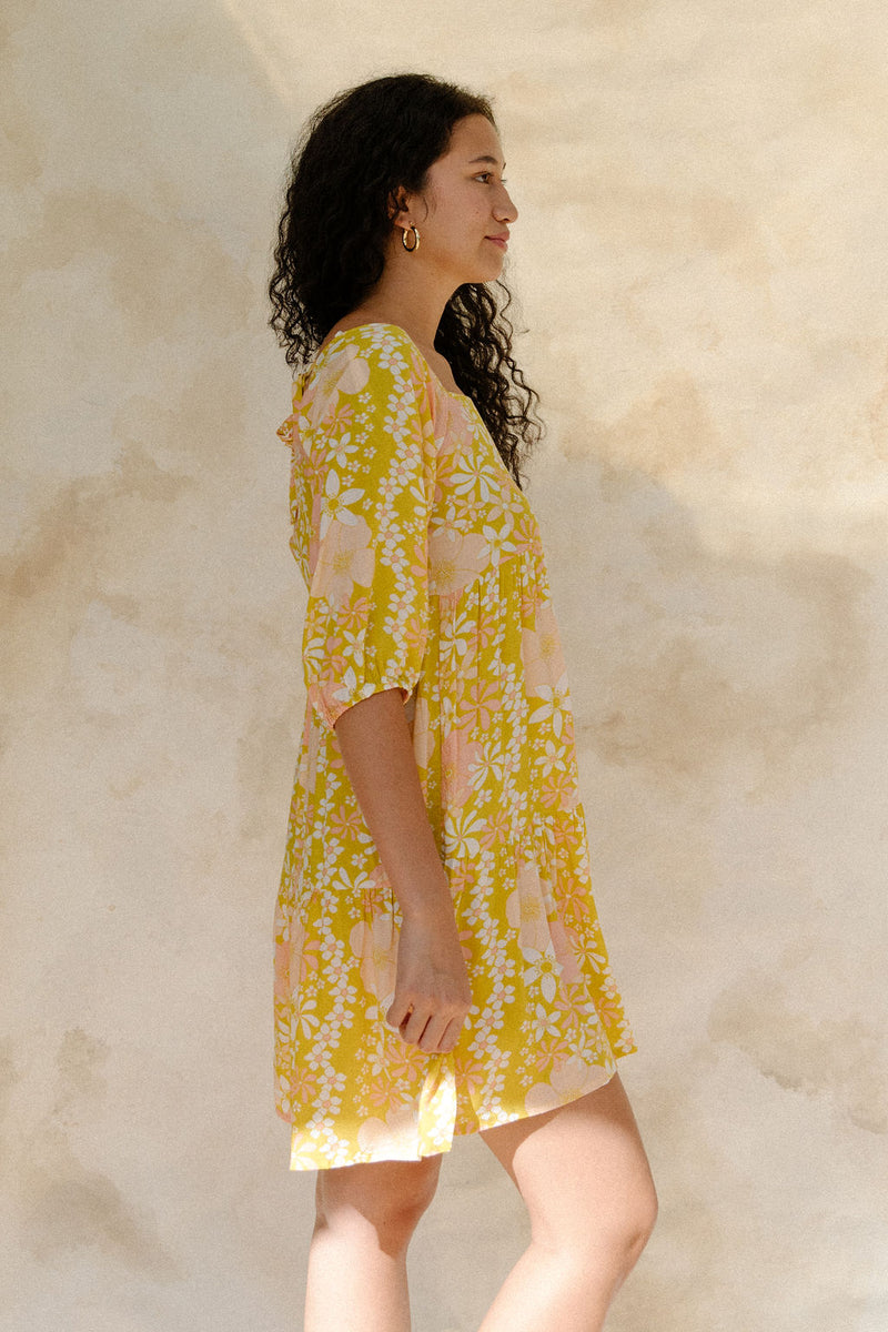 Woman in short flowy tiered dress with 3/4 sleeves in white and peach floral print with yellow ground.