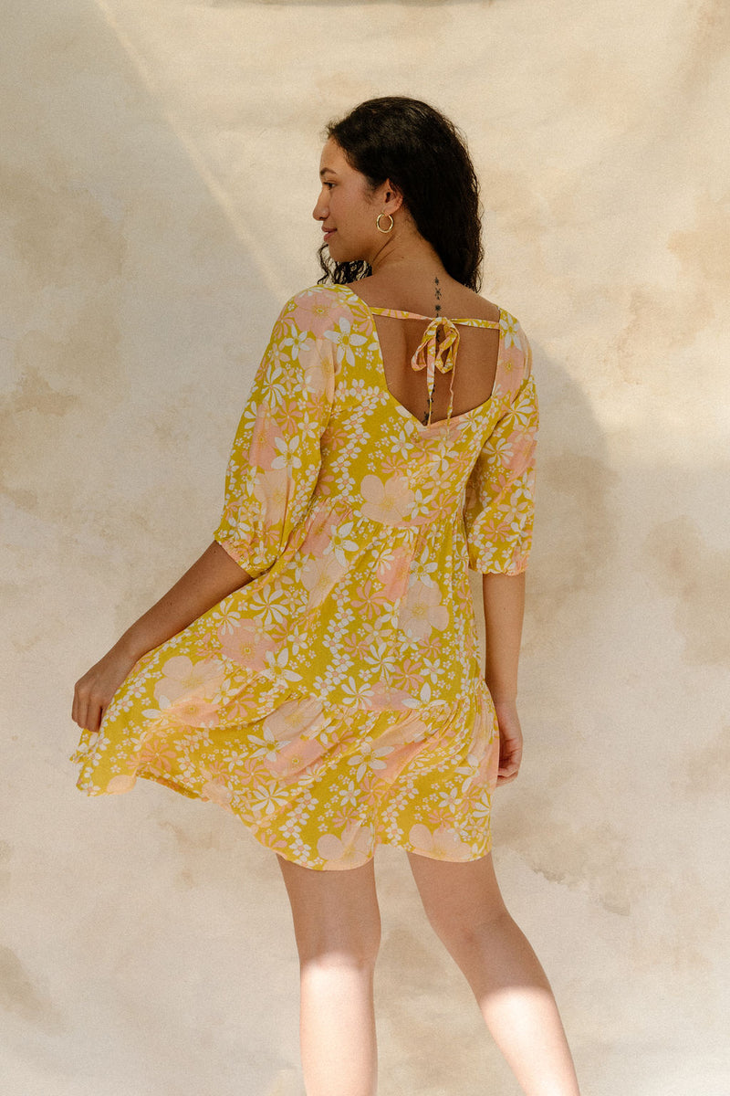 Woman in short flowy tiered dress with 3/4 sleeves in white and peach floral print with yellow ground.