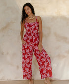 Woman in sleeveless jumpsuit in pink floral print with red background.