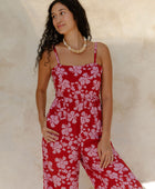 Woman in sleeveless jumpsuit in pink floral print with red background.