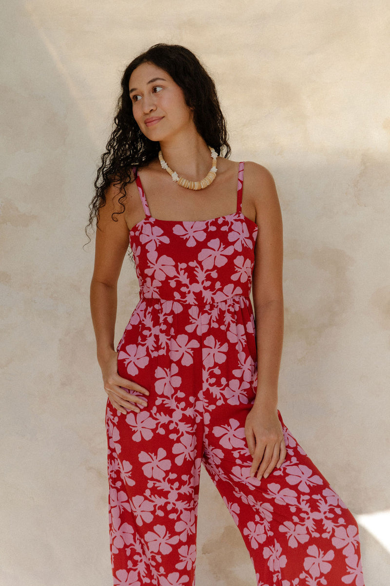 Woman in sleeveless jumpsuit in pink floral print with red background.