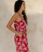 Woman in sleeveless jumpsuit in pink floral print with red background.