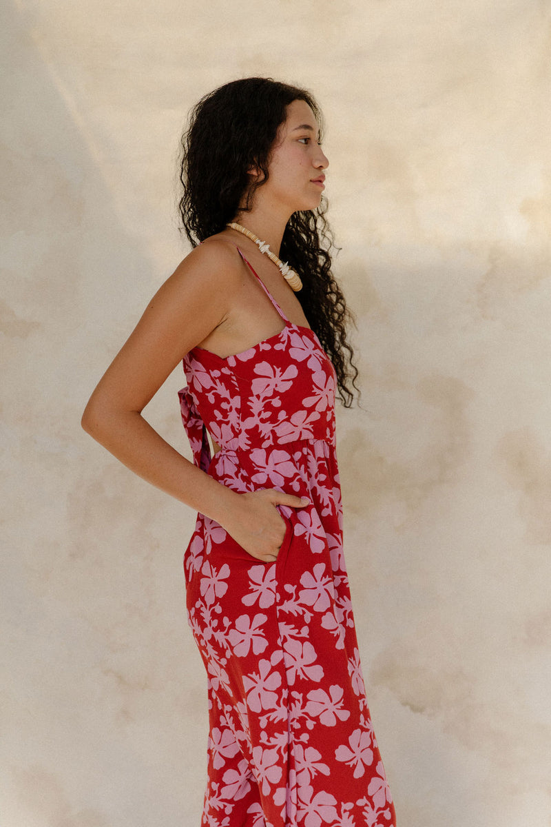 Woman in sleeveless jumpsuit in pink floral print with red background.