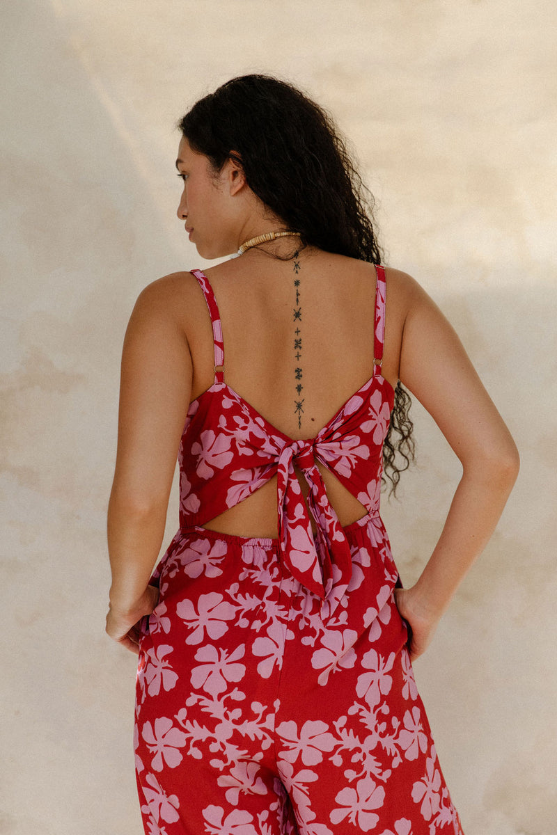 Woman in sleeveless jumpsuit in pink floral print with red background.