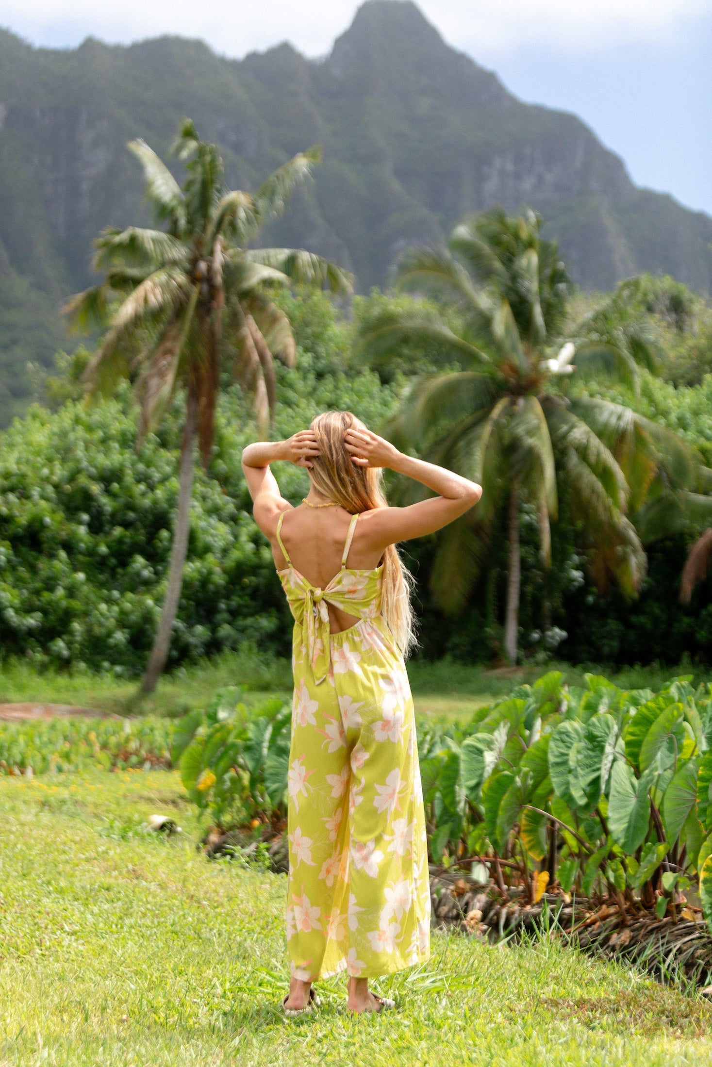 woman wearing a bright green tie back jumpsuit with orchid print