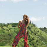 woman with brown hair wearing a colorful jumpsuit with tropical lei print