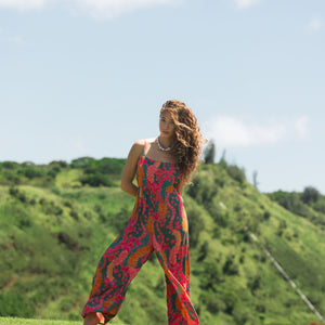 woman with brown hair wearing a colorful jumpsuit with tropical lei print