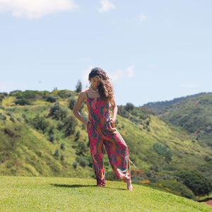 woman with brown hair wearing a colorful jumpsuit with tropical lei print