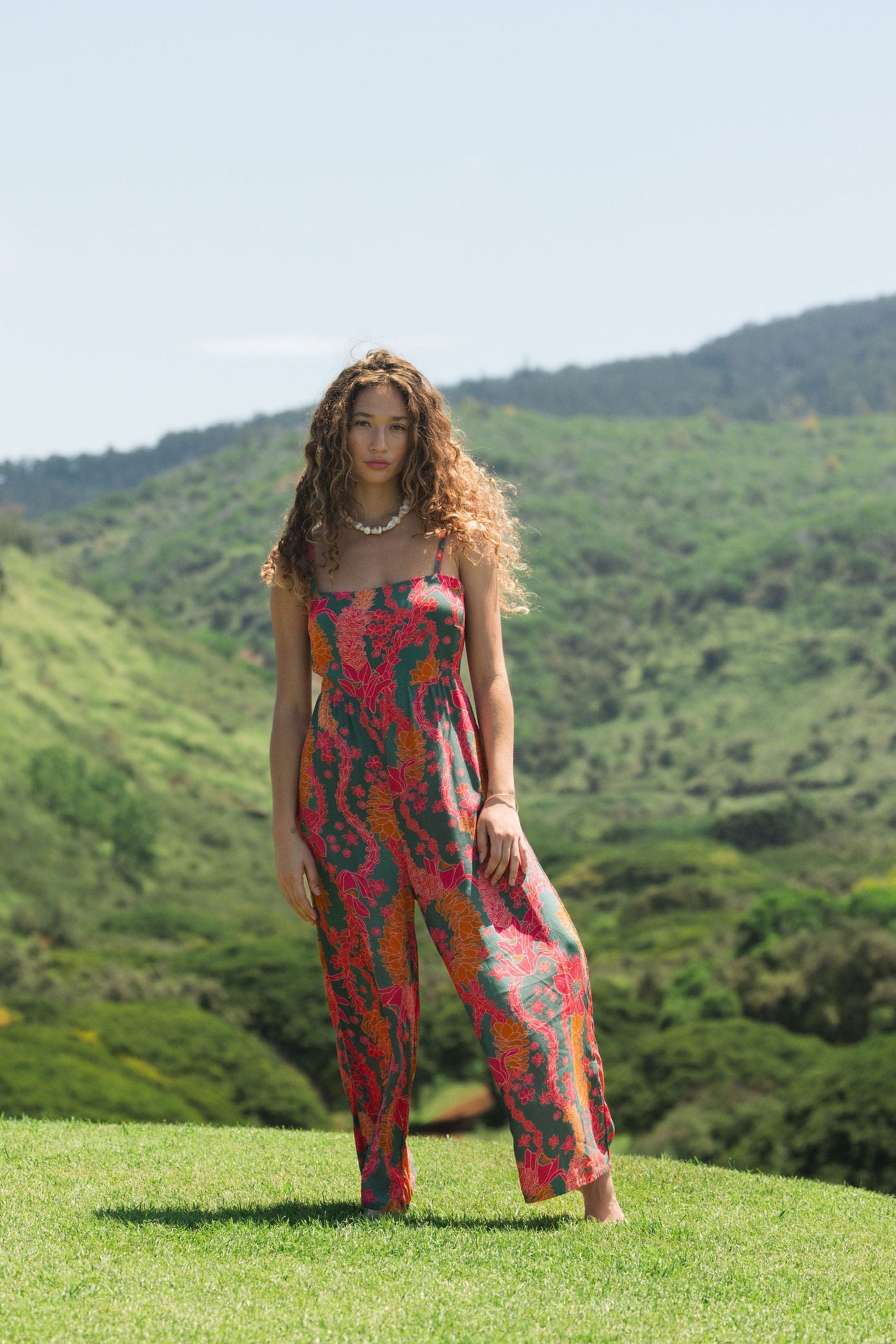 woman with brown hair wearing a colorful jumpsuit with tropical lei print
