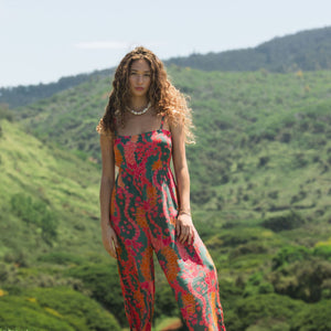 woman with brown hair wearing a colorful jumpsuit with tropical lei print