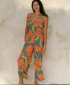 Woman in sleeveless jumpsuit in large orange floral print with green background.