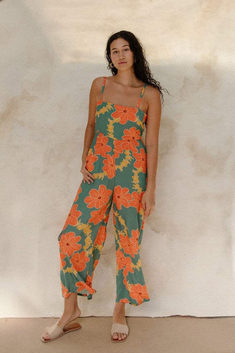 Woman in sleeveless jumpsuit in large orange floral print with green background.