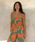 Woman in sleeveless jumpsuit in large orange floral print with green background.