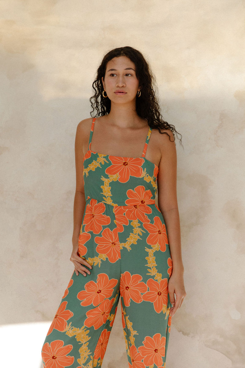 Woman in sleeveless jumpsuit in large orange floral print with green background.