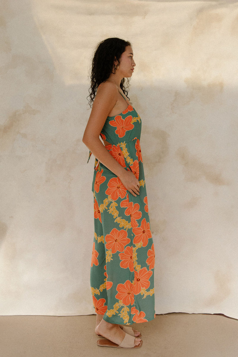 Woman in sleeveless jumpsuit in large orange floral print with green background.