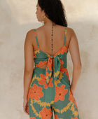 Woman in sleeveless jumpsuit in large orange floral print with green background.