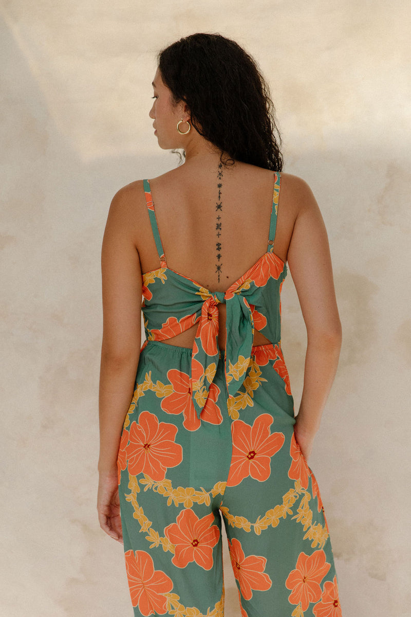 Woman in sleeveless jumpsuit in large orange floral print with green background.