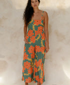 Woman in sleeveless jumpsuit in large orange floral print with green background.