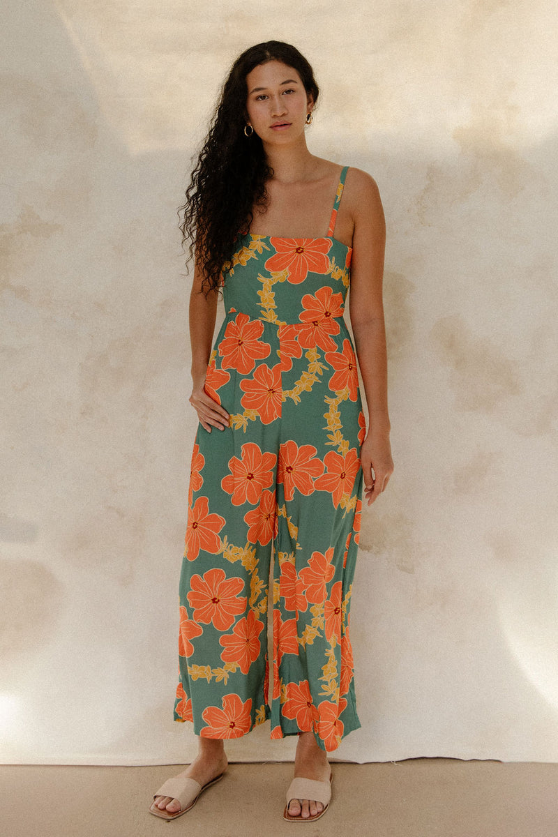 Woman in sleeveless jumpsuit in large orange floral print with green background.