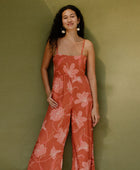 Woman in long sleeveless jumpsuit with rust colored floral print.