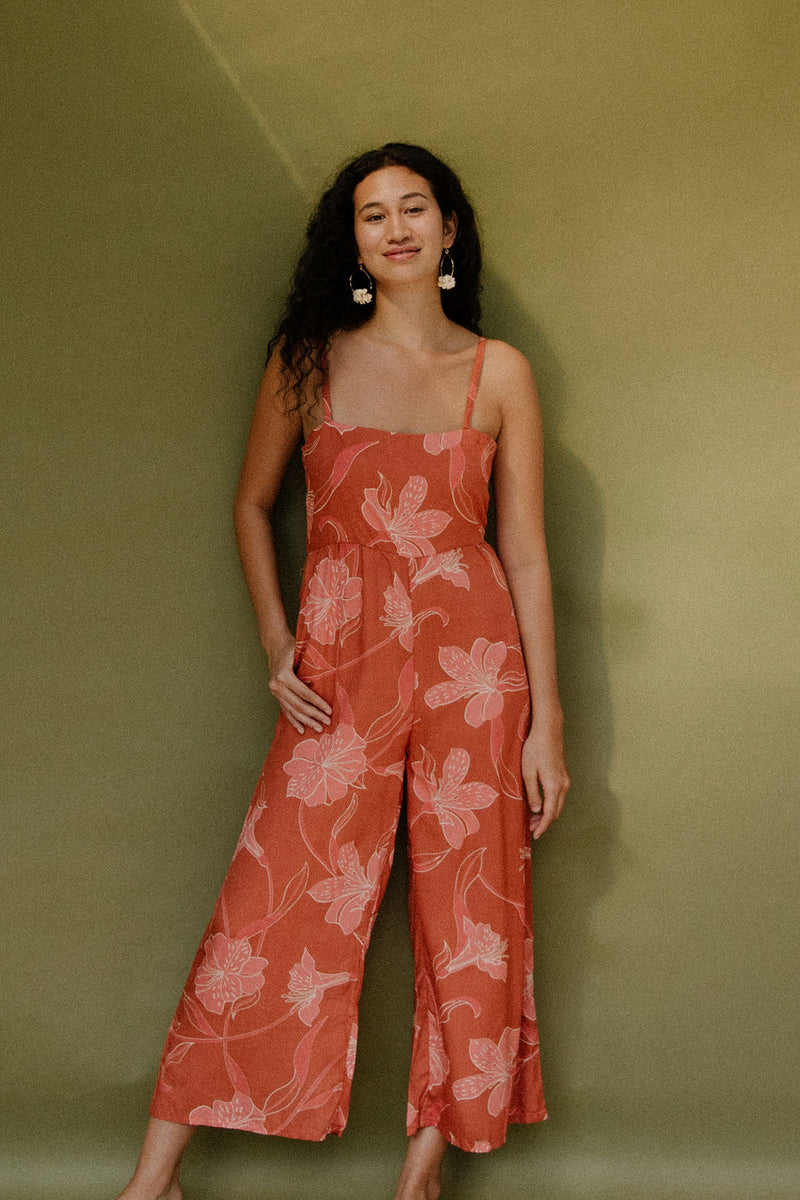 Woman in long sleeveless jumpsuit with rust colored floral print.