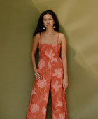 Woman in long sleeveless jumpsuit with rust colored floral print.