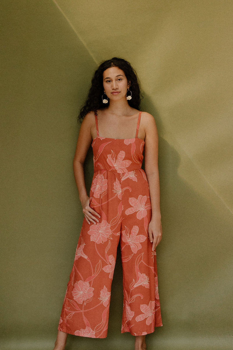 Woman in long sleeveless jumpsuit with rust colored floral print.