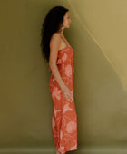 Woman in long sleeveless jumpsuit with rust colored floral print.