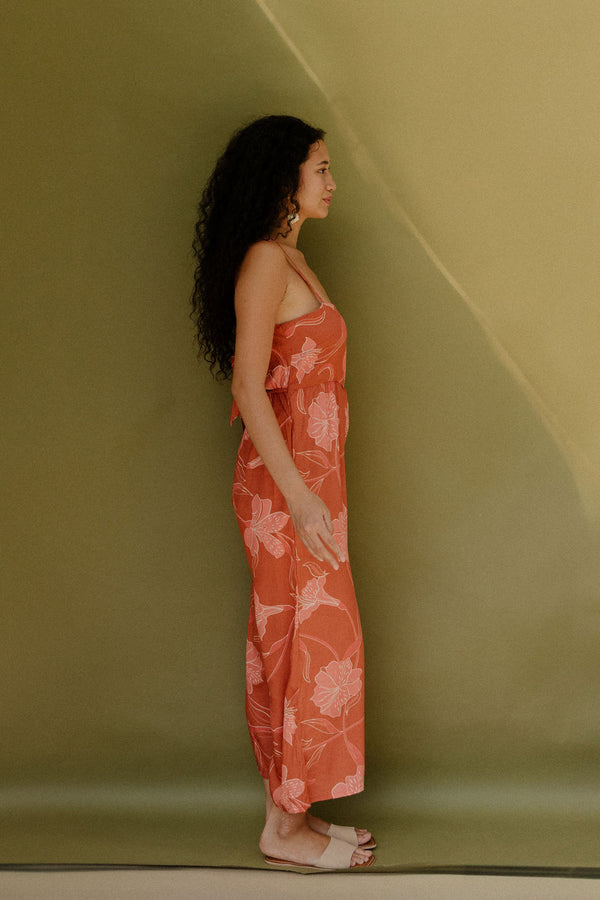 Woman in long sleeveless jumpsuit with rust colored floral print.