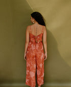 Woman in long sleeveless jumpsuit with rust colored floral print.