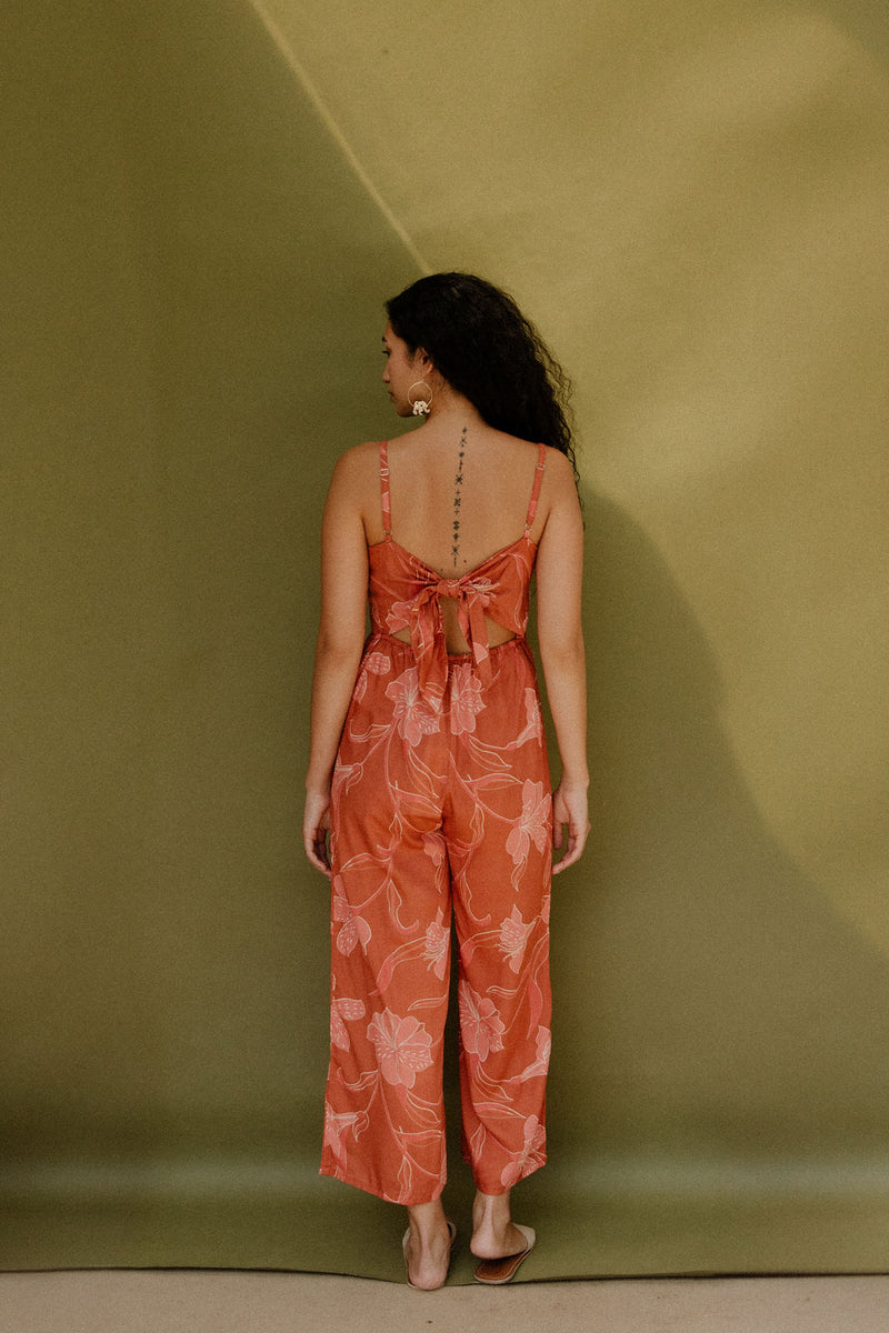 Woman in long sleeveless jumpsuit with rust colored floral print.